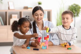 A woman playing with building blocks with two children