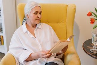 An older woman enjoys reading a good book in her yellow chair. 