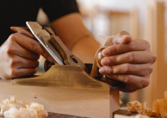 A developing furniture maker is carving wood into a desired shape.