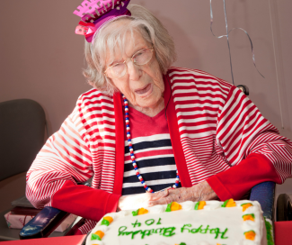 An older woman celebrates her 104th birthday. A cake is in front of her and a present is behind her. 