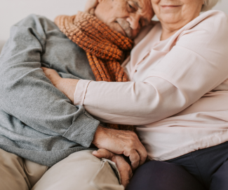 An older couple sit and share an embrace. 