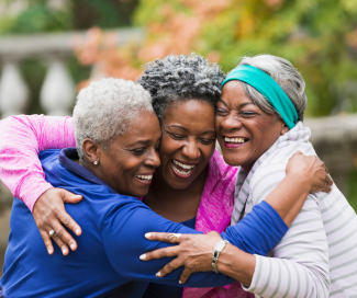 Three, smiling older women hug each other outside.  