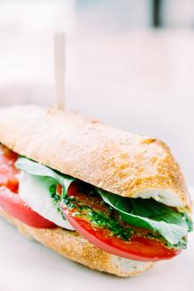 A footlong, healthy sandwich with spinach, tomatoes, pesto sauce and cheese.