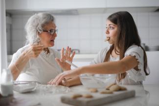 A grandmother and her granddaughter have a conversation while baking cookies.