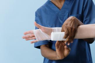 A nursing student practices bandaging a wrist and hand. 