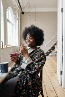 A woman eating from a bowl of mixed berries in her apartment. 