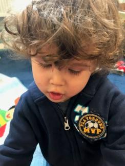 A close up of a little boy with big hair and a navy blue hoodie. 