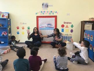 Two child care teachers sing along and perform with their students.