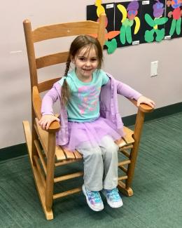 A little girl with a purple tutu sits in a rocking chair at a Rhode Island child care site.