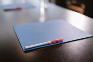A blue folder and pen sits on a desk.