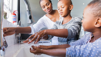 A mom and her two kids wash their hands together. 