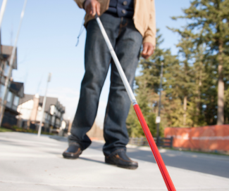 The legs of a blind man with his cane as he walks down the street.