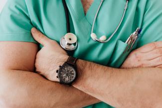 A close up on a doctor with a stethoscope folding his arms across his chest.