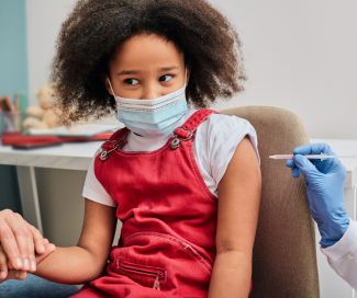 A young girl wearing a mask gets vaccinated
